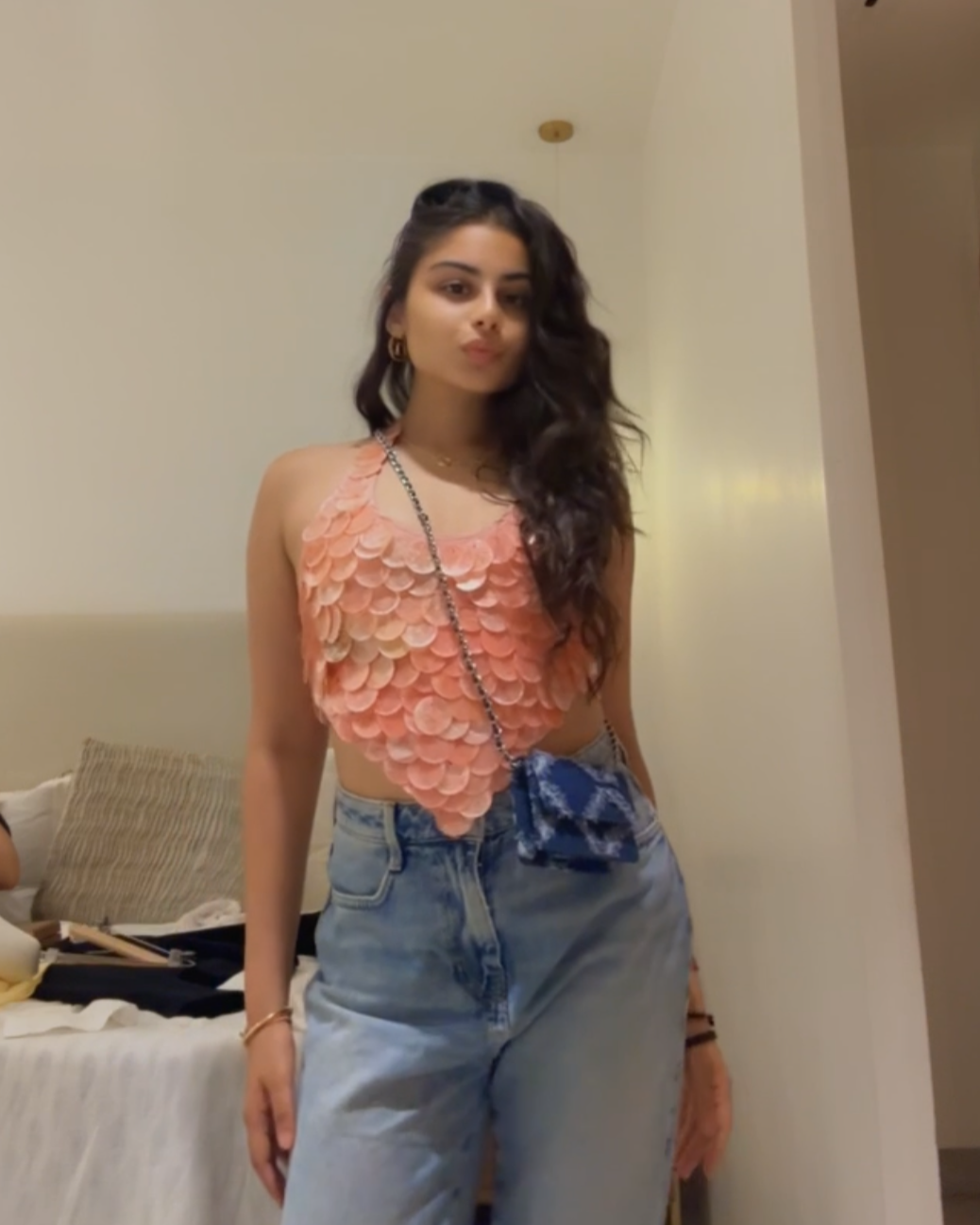 Woman wearing a pink shell top and blue jeans standing in a room.